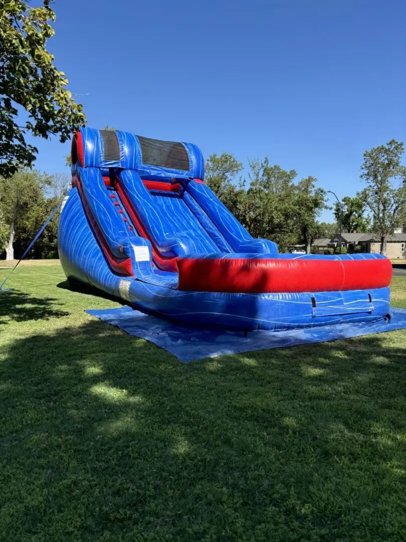 A blue and red inflatable slide in the grass.